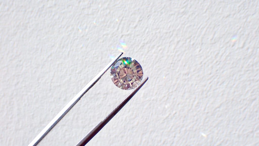 Tweezers holding a cut diamond against a gray background