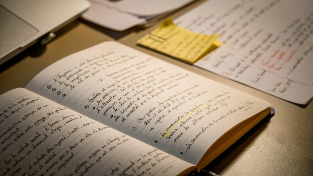 Image of a desk. Visible are a notebook with writing in French and some other papers.