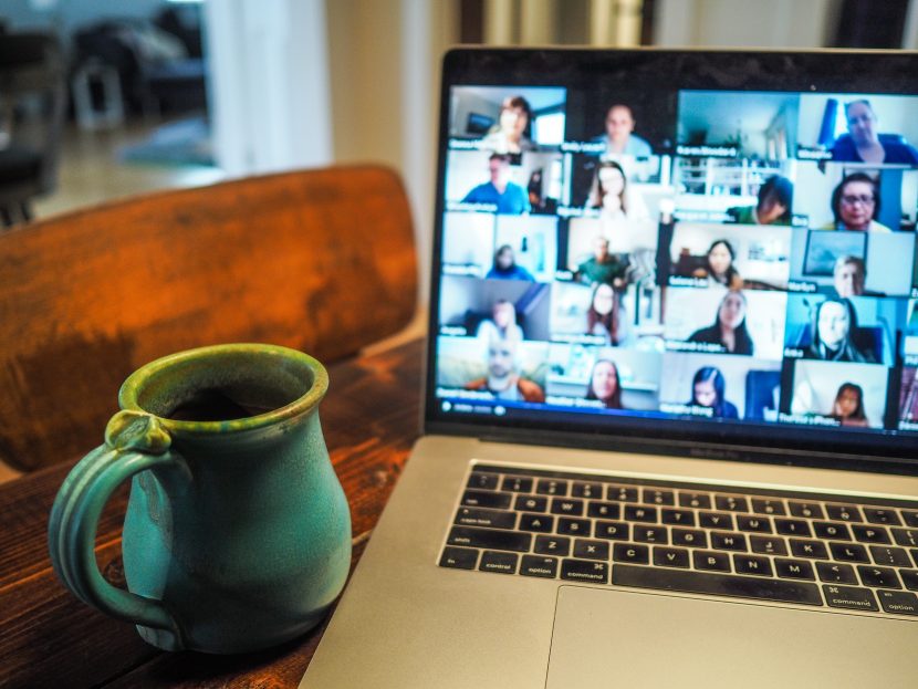 Coffee mug next to an open laptop showing numerous online attendees of a meeting